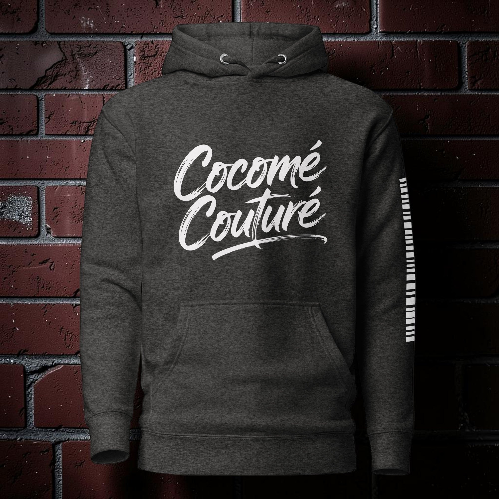 CocoMe Couture charcoal heather premium hoodie with white logo print and kangaroo pocket against a brick wall