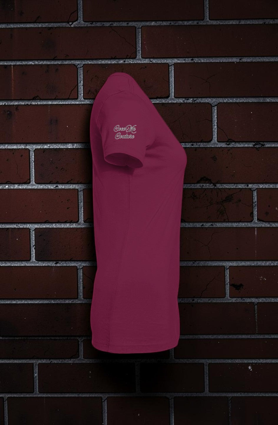 Side view of a maroon CocoMe Couture slim-fit women's graphic tee featuring a logo on the sleeve against a brick wall