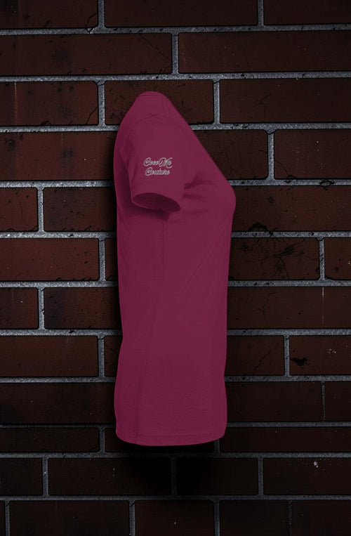 Side view of a maroon CocoMe Couture slim-fit women's graphic tee featuring a logo on the sleeve against a brick wall