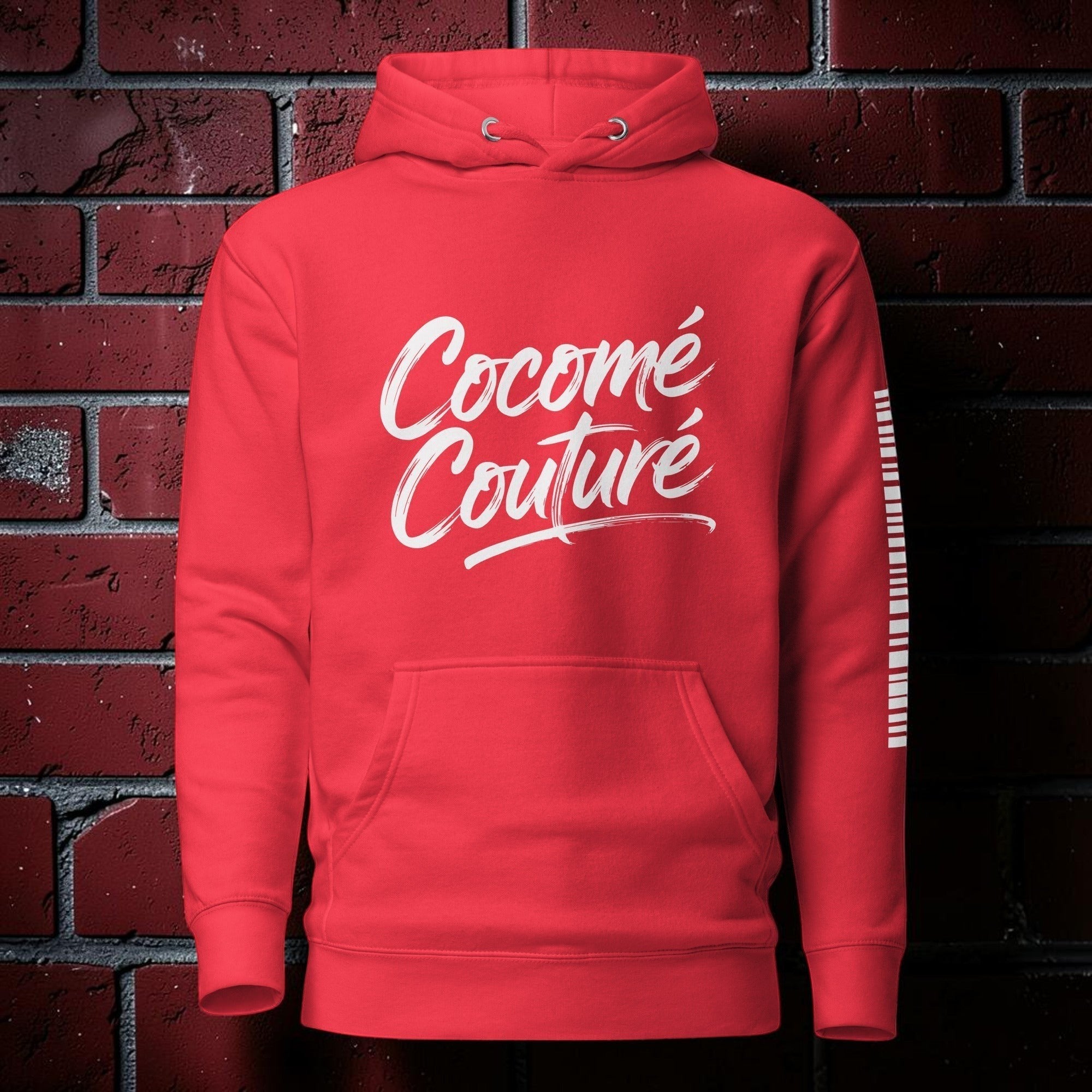 CocoMe Couture red premium unisex pullover hoodie with white script logo and kangaroo pocket against brick wall