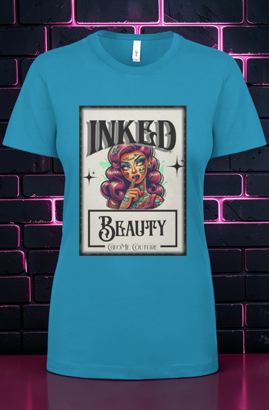 CocoMe Couture turquoise crewneck t-shirt featuring an Inked Beauty graphic print on a dark neon brick background.